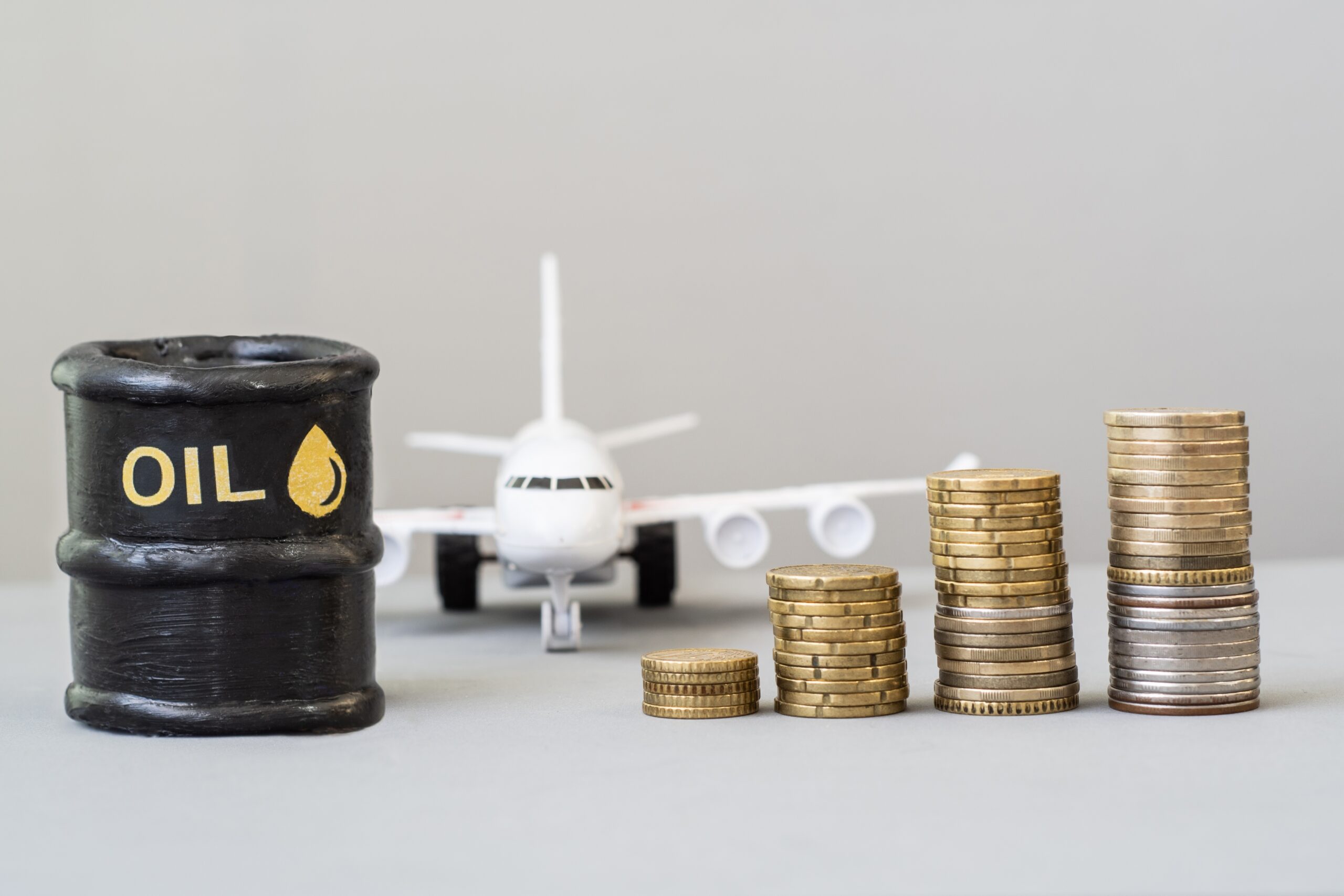 OilBarrelWithAnAirplaneAndGrowingStacksOfCoins - USA Works Oil drum labeled OIL with a toy airplane and stacks of coins in the foreground, illustrating fuel costs and travel expenses.