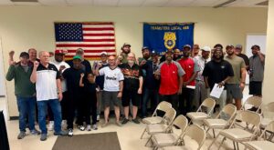 CocaCola-688jpg - USA Works - USA Works Group of diverse people posing with raised fists in a room, flags (US flag and Teamsters Local 688) in the background, a formal, celebratory gathering.